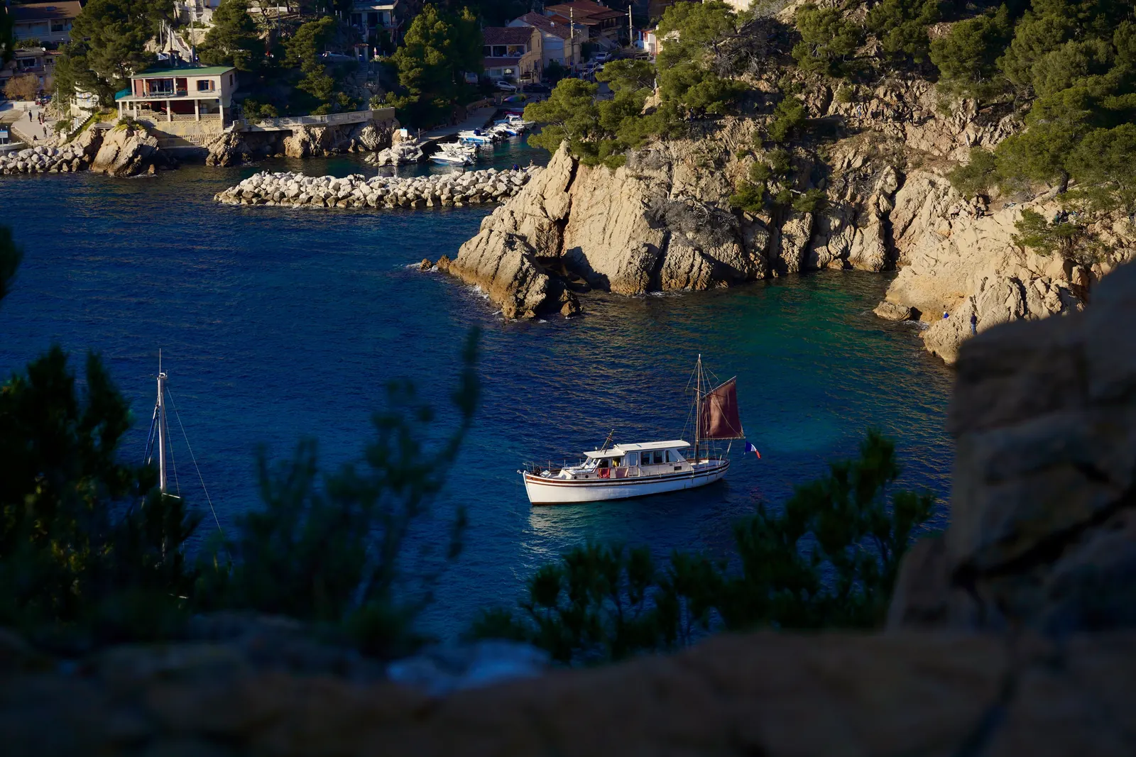 A small boat at anchor in a calanque, pine trees and limestone cliffs around the turquoise water