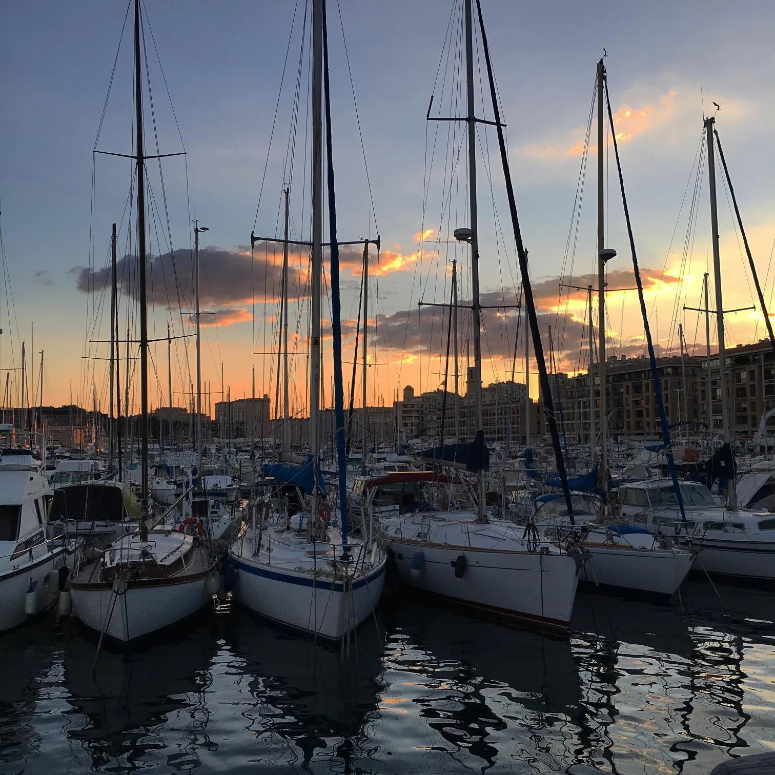 Sailing boats moored in Marseille at sunset, masts against an orange sky